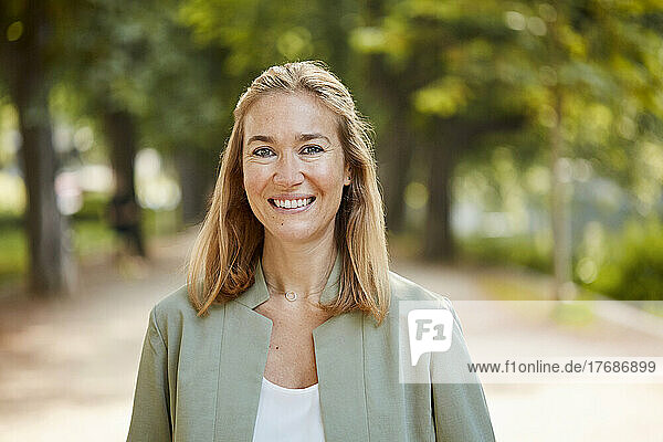Smiling blond woman wearing jacket standing in park