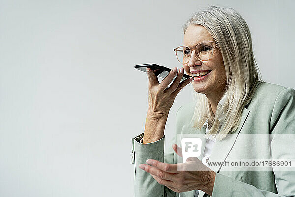 Businesswoman talking on speaker phone against white background