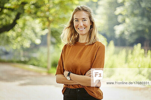 Happy woman with arms crossed standing in park