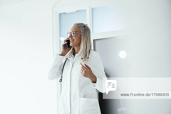 Smiling senior female doctor talking on smart phone at hospital