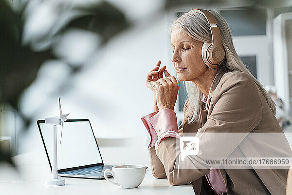 Businesswoman listening music with eyes closed at desk in office