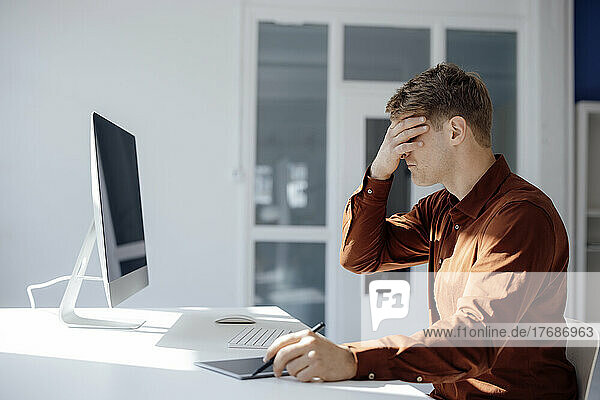 Businessman covering eyes with hands sitting at desk in office