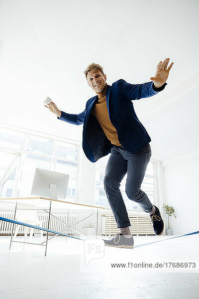 Happy businessman balancing on tightrope in office