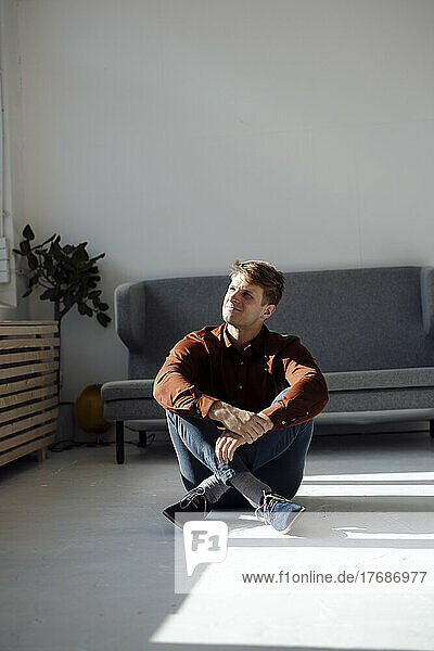 Smiling man sitting on floor in front of sofa in living room at home