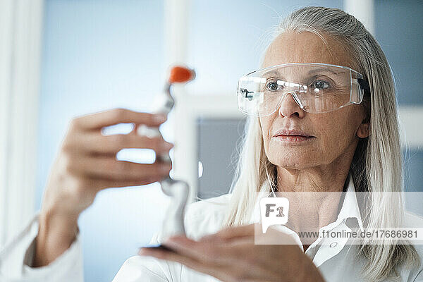 Engineer with protective eyewear looking at robotic arm in workshop