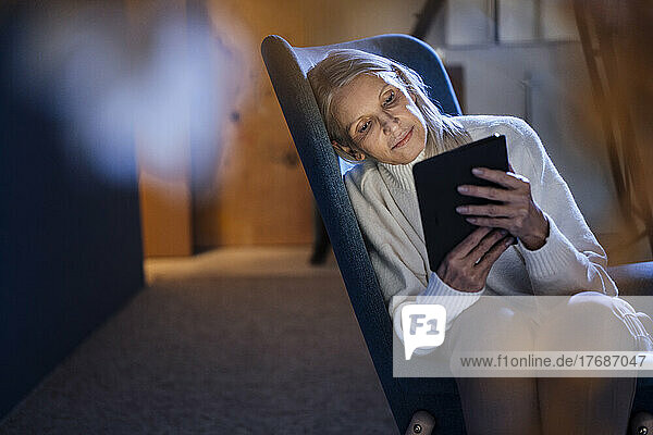 Senior woman using tablet PC resting on chair