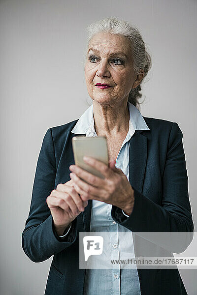 Businesswoman with smart phone standing against white background