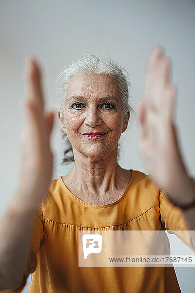 Smiling woman with gray hair gesturing with hand against white background
