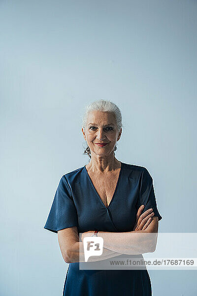 Smiling senior woman with arms crossed standing against white background