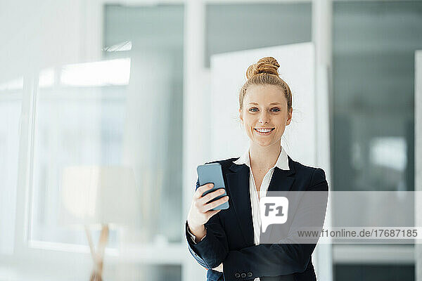Geschäftsfrau mit Haarknoten hält Smartphone im Büro