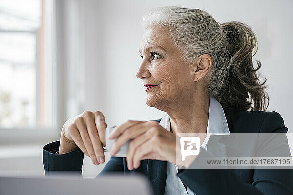 Smiling businesswoman with coffee cup sitting in office