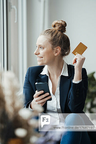 Betrachtet eine Geschäftsfrau mit Smartphone und Kreditkarte im Büro