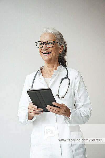 Happy senior doctor with tablet PC standing against white background