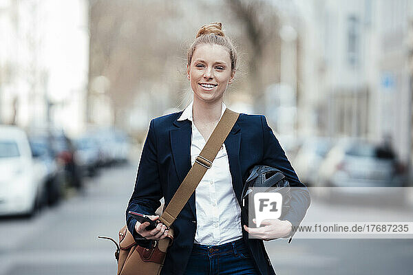 Smiling businesswoman holding helmet and smart phone