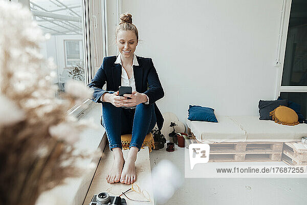 Lächelnde Geschäftsfrau  die im Büro SMS über ihr Smartphone sendet