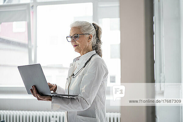 Arzt mit Brille und Laptop am Fenster