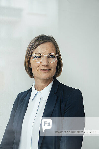 Reife Geschäftsfrau mit Brille vor weißer Wand