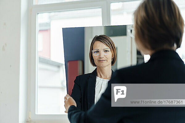 Businesswoman looking through mirror reflection at office