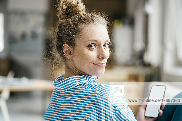 Smiling freelancer looking over shoulder holding smart phone