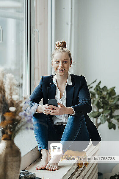 Junge Geschäftsfrau mit Smartphone sitzt im Büro