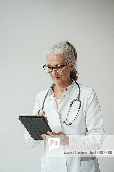Senior doctor using tablet PC standing against white background