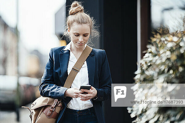 Businesswoman with shoulder bag using smart phone