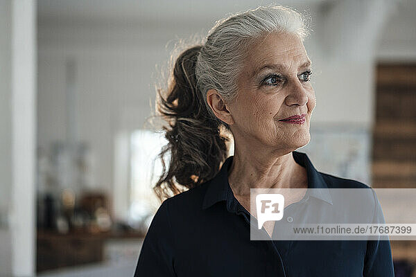 Thoughtful smiling businesswoman with gray hair in office