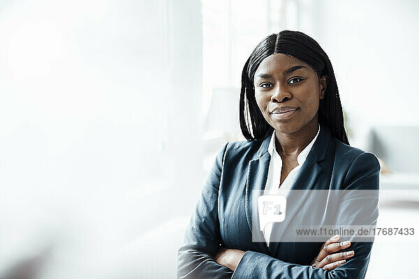 Smiling businesswoman standing with arms crossed at office