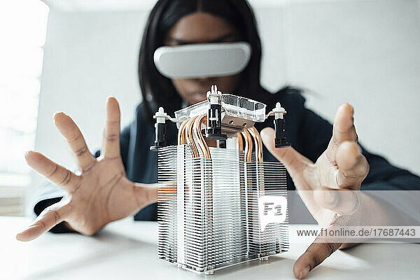 Engineer wearing virtual reality simulator gesturing at semiconductor on desk in office