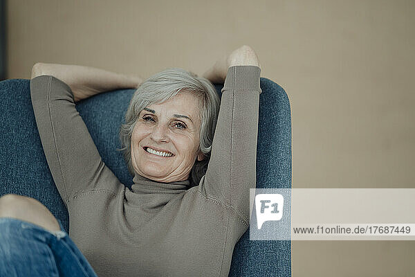 Happy senior woman sitting on chair in front of wall