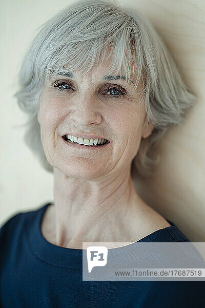 Smiling senior woman with gray hair in front of wall