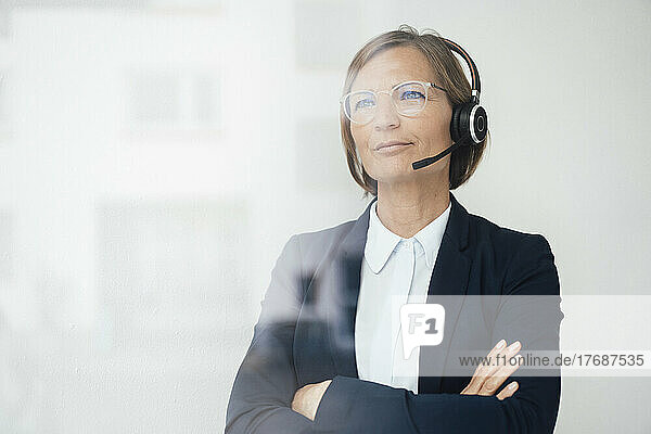 Thoughtful businesswoman with arms crossed looking through glass window