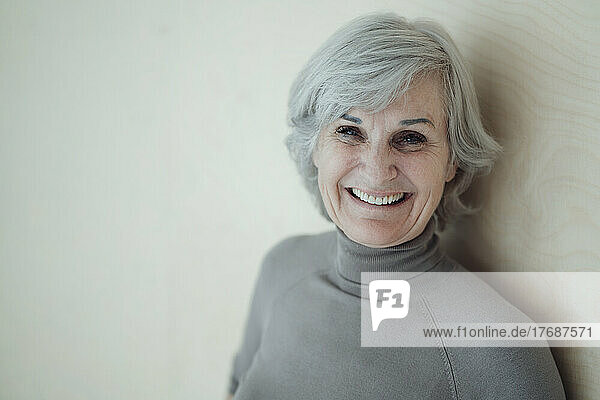 Happy senior woman standing in front of wall