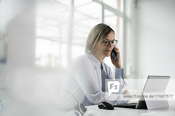 Businesswoman talking on mobile phone sitting at desk in office
