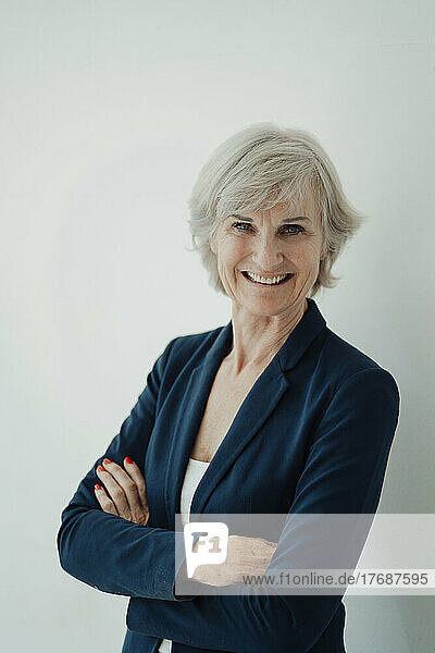 Happy businesswoman with arms crossed standing against white background