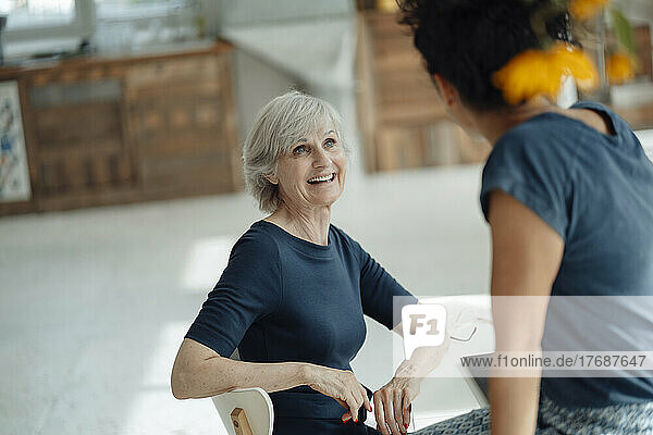 Happy senior businesswoman discussing with colleague sitting on desk in office