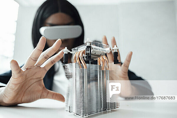 Engineer wearing virtual reality simulator gesturing at machine part on desk