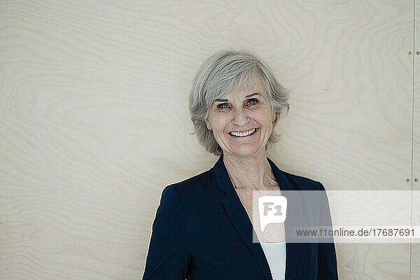 Happy businesswoman with gray hair standing in front of wall