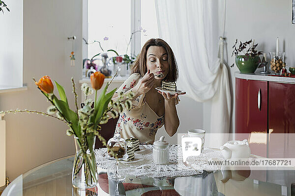 Happy woman eating slice of cake sitting at dining table