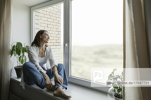 Happy mature woman sitting on window sill at home