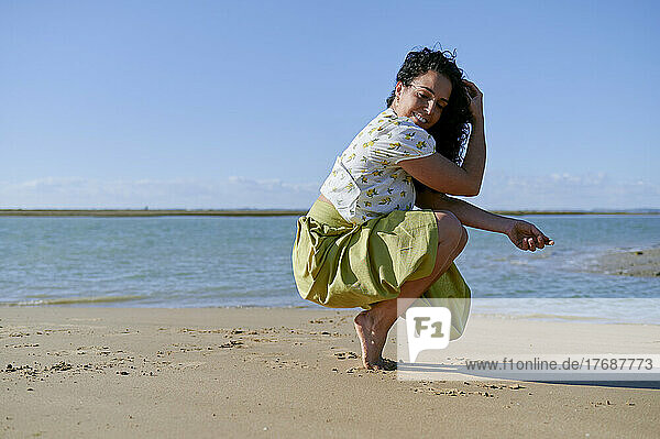 Smiling young woman crouching on tiptoe on shore at beach
