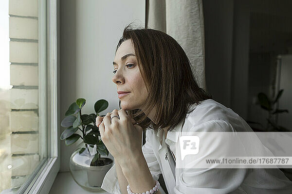 Mature woman with brown hair looking through window at home