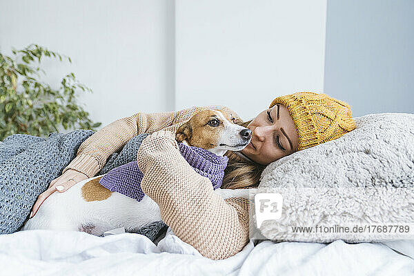 Woman wearing warm clothing cuddling with dog in bed