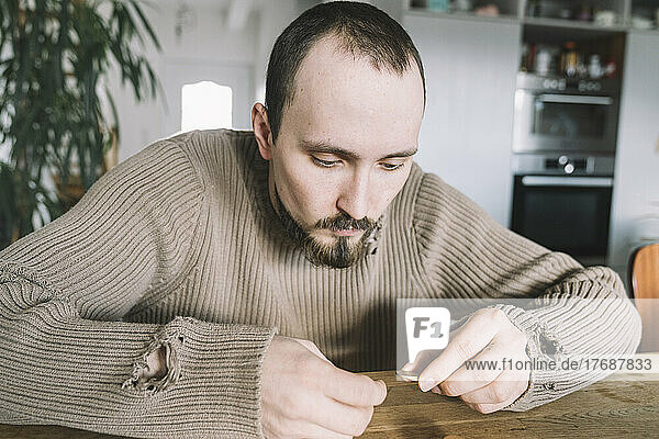 Young man with torn pullover sitting at home counting money