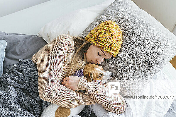 Woman wearing warm clothing cuddling with dog in bed