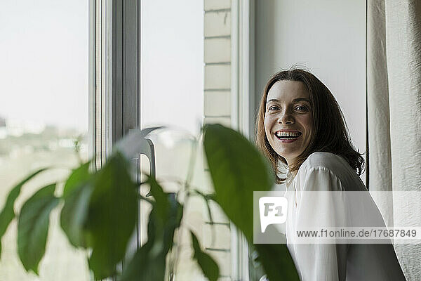 Happy mature woman standing by window at home