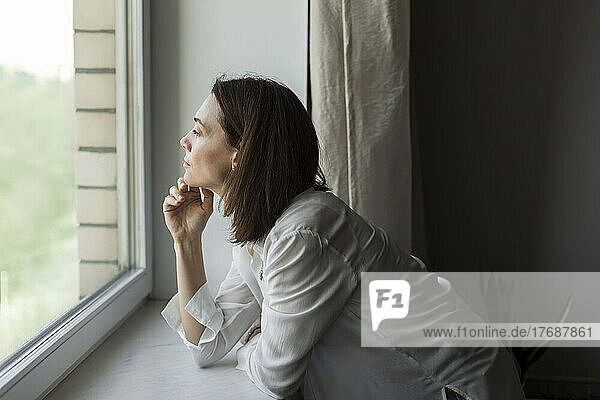 Mature woman with hand on chin looking through window at home