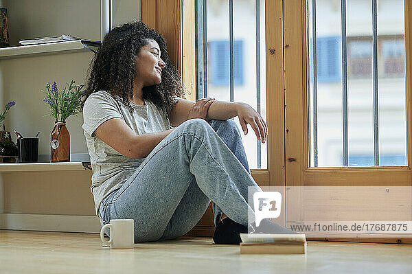 Smiling woman looking through glass door sitting on floor at home