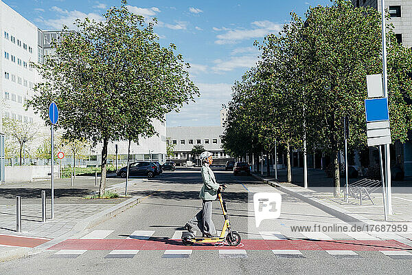 Businesswoman crossing road with electric push scooter