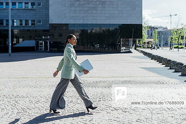 Confident businesswoman with laptop walking by office building